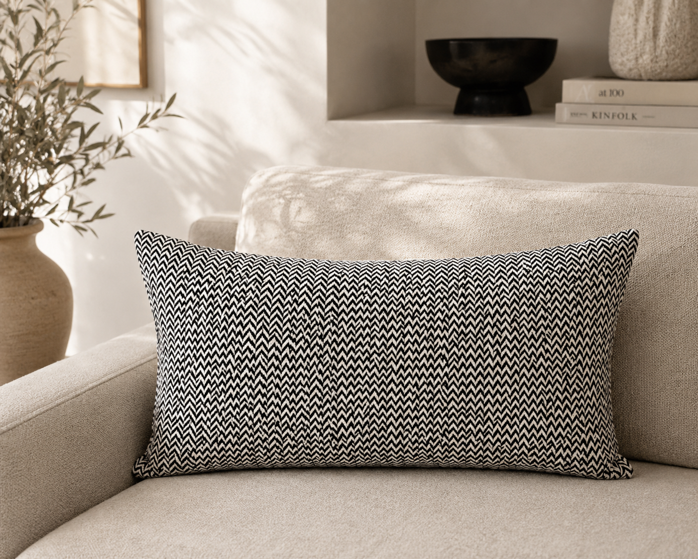 Coussin rectangulaire noir et blanc à motif chevron dans une ambiance minimaliste chic avec canapé beige, décoration contemporaine et lumière naturelle chaleureuse.