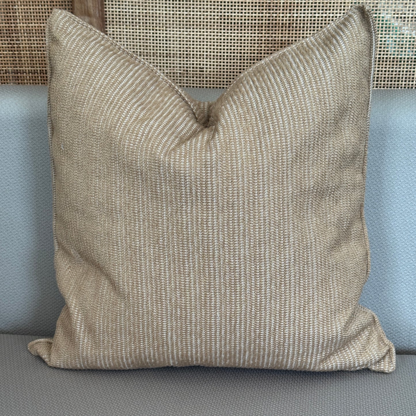 Coussin beige à fines rayures blanches posé sur un canapé taupe .