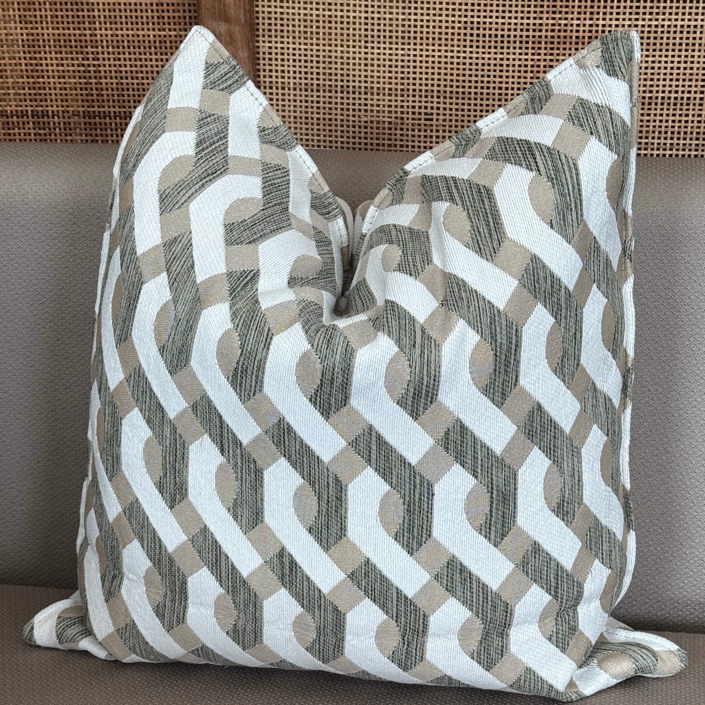 Coussin décoratif à motif géométrique beige, blanc et vert posé sur un canapé.