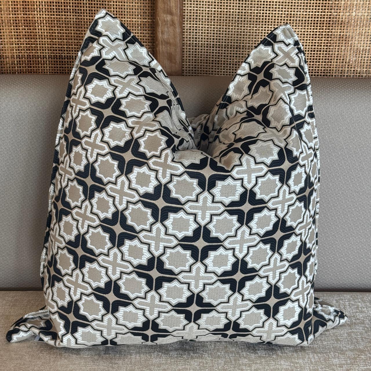 Coussin décoratif à motif géométrique marocain en noir, beige et blanc cassé, tissu tissé en relief avec finition élégante, posé sur un canapé beige.
