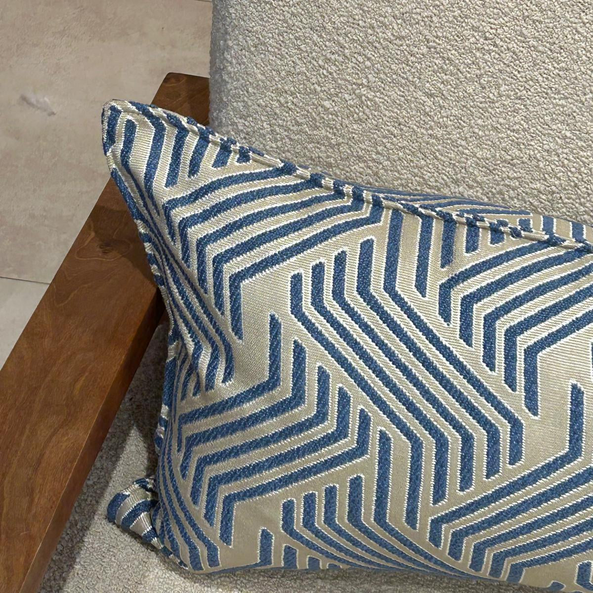Détail d’un coussin rectangulaire à motif graphique bleu et écru en tissu texturé, finition soignée, posé sur fauteuil clair