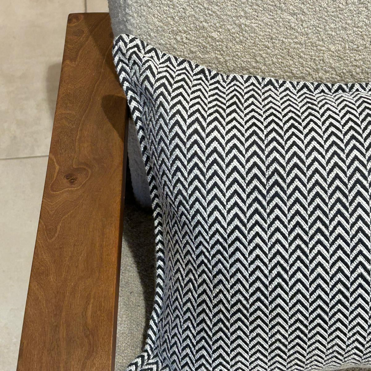 Détail d’un coussin à motif chevron noir et blanc en tissu texturé, finition soignée, posé sur fauteuil clair en bouclette
