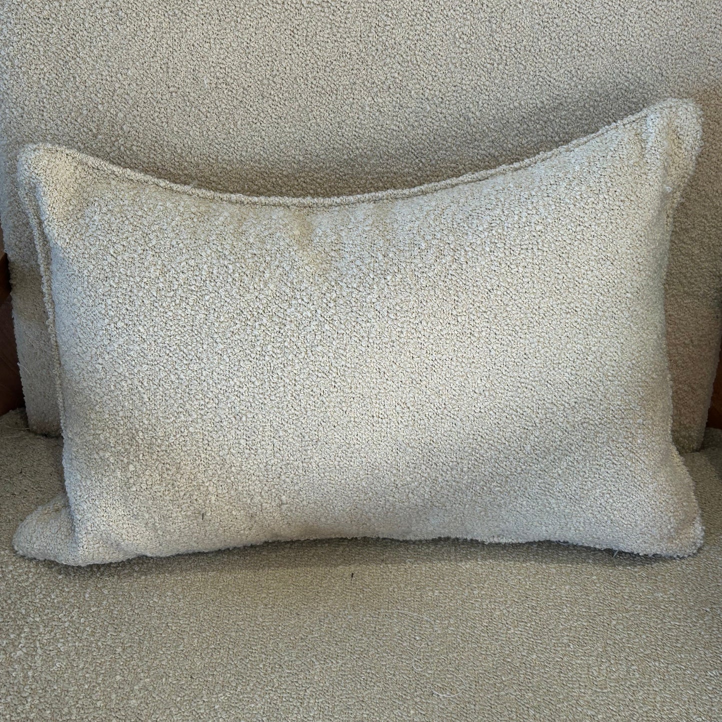 Coussin rectangulaire en tissu bouclette écru, texture douce, posé sur fauteuil clair