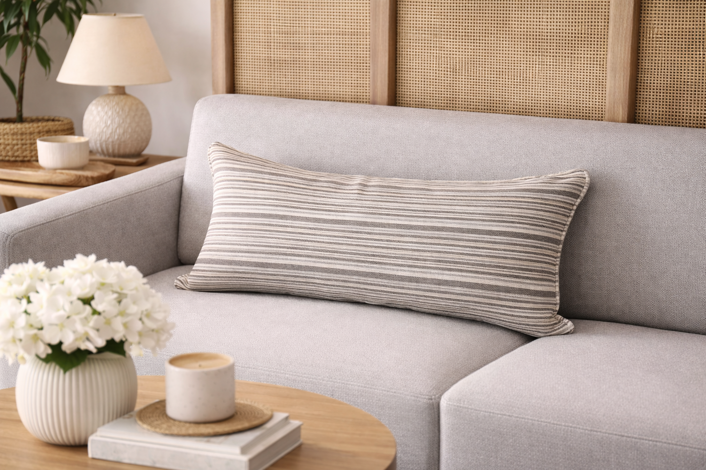 Coussin rectangulaire à rayures taupe et écru posé sur un canapé clair dans une ambiance salon lumineuse et haut de gamme
