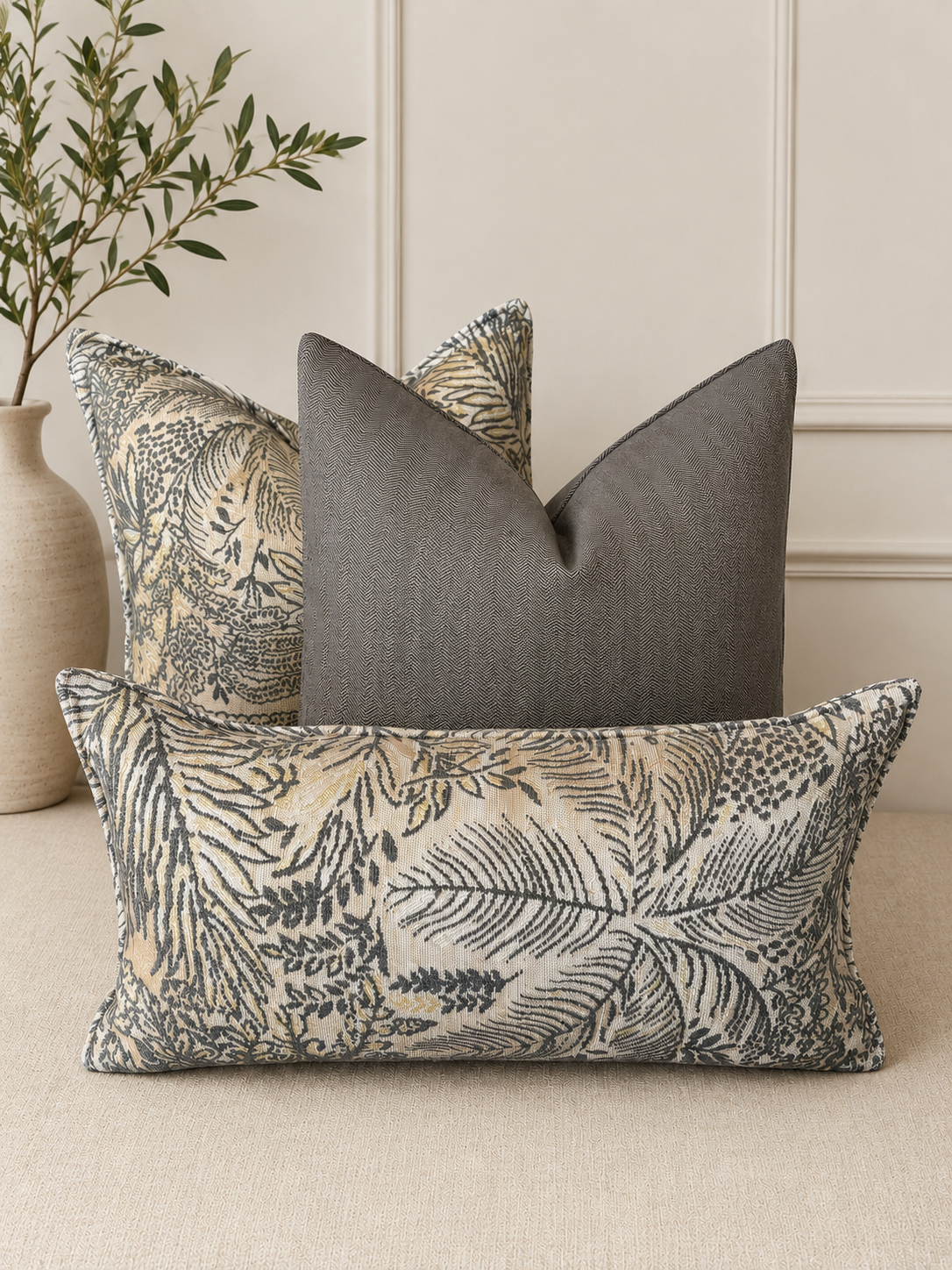 Coussins décoratifs en tissu tissé au Maroc, motif feuillage gris et beige, disposés sur un canapé dans un salon moderne et élégant.