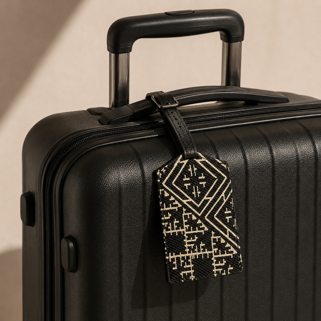Étiquette bagage Tarz Noir Biyadi Collection en cuir véritable et tissu tissé au Maroc, accrochée à une valise noire.