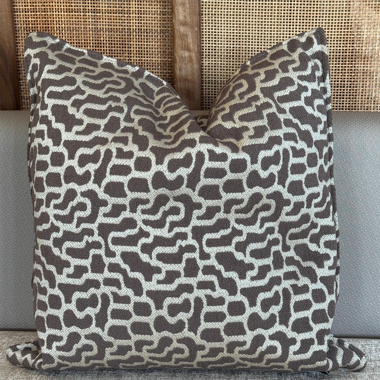 Coussin décoratif taupe avec motif abstrait en relief, au style moderne et graphique.