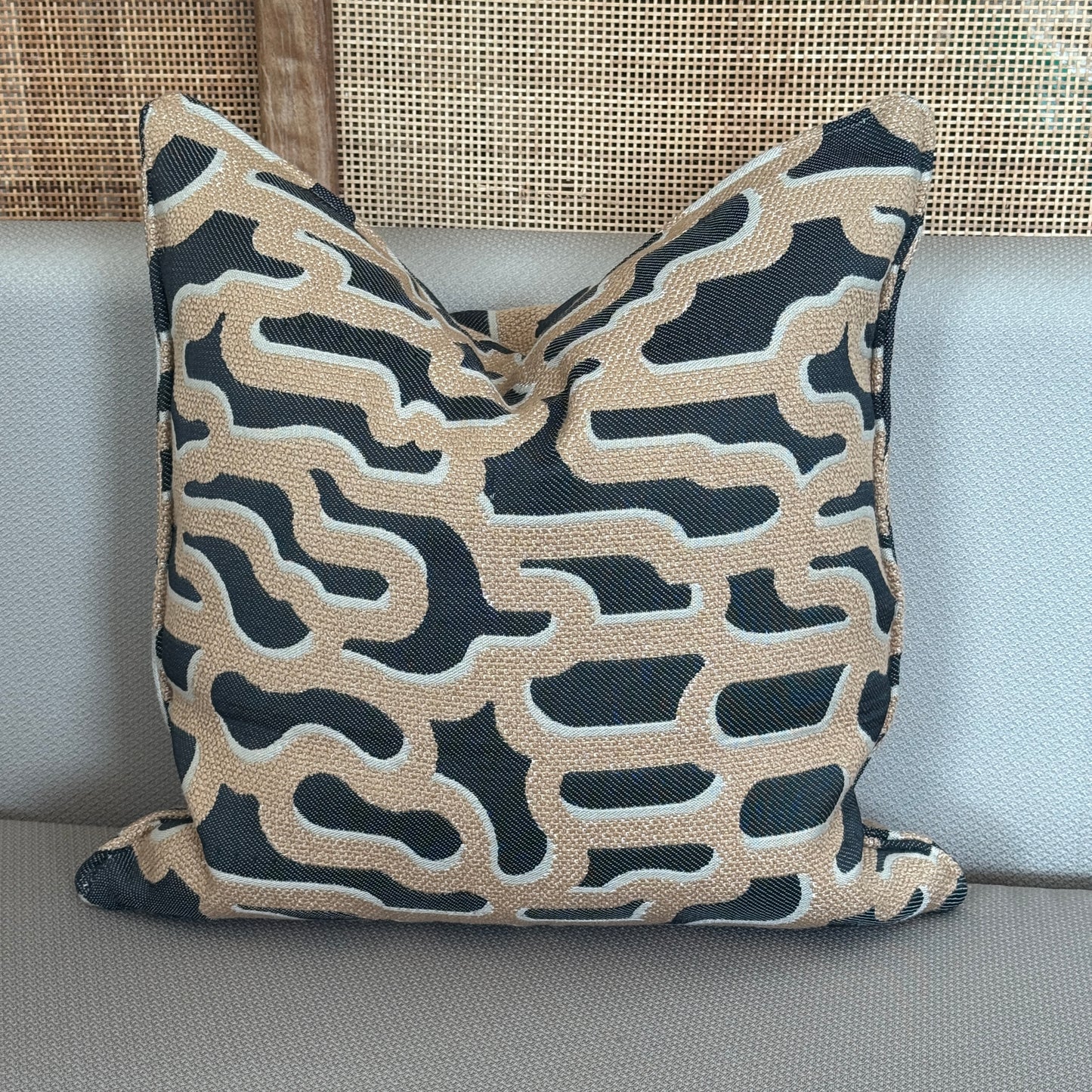  Coussin décoratif avec motifs abstraits beige et noir posé sur un canapé.