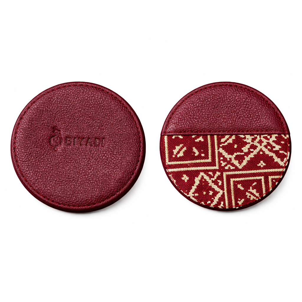 Sous-tasse ronde double face, avec une face en cuir bordeau portant le logo Biyadi embossé et une face en tissu Tarz noir et écru.