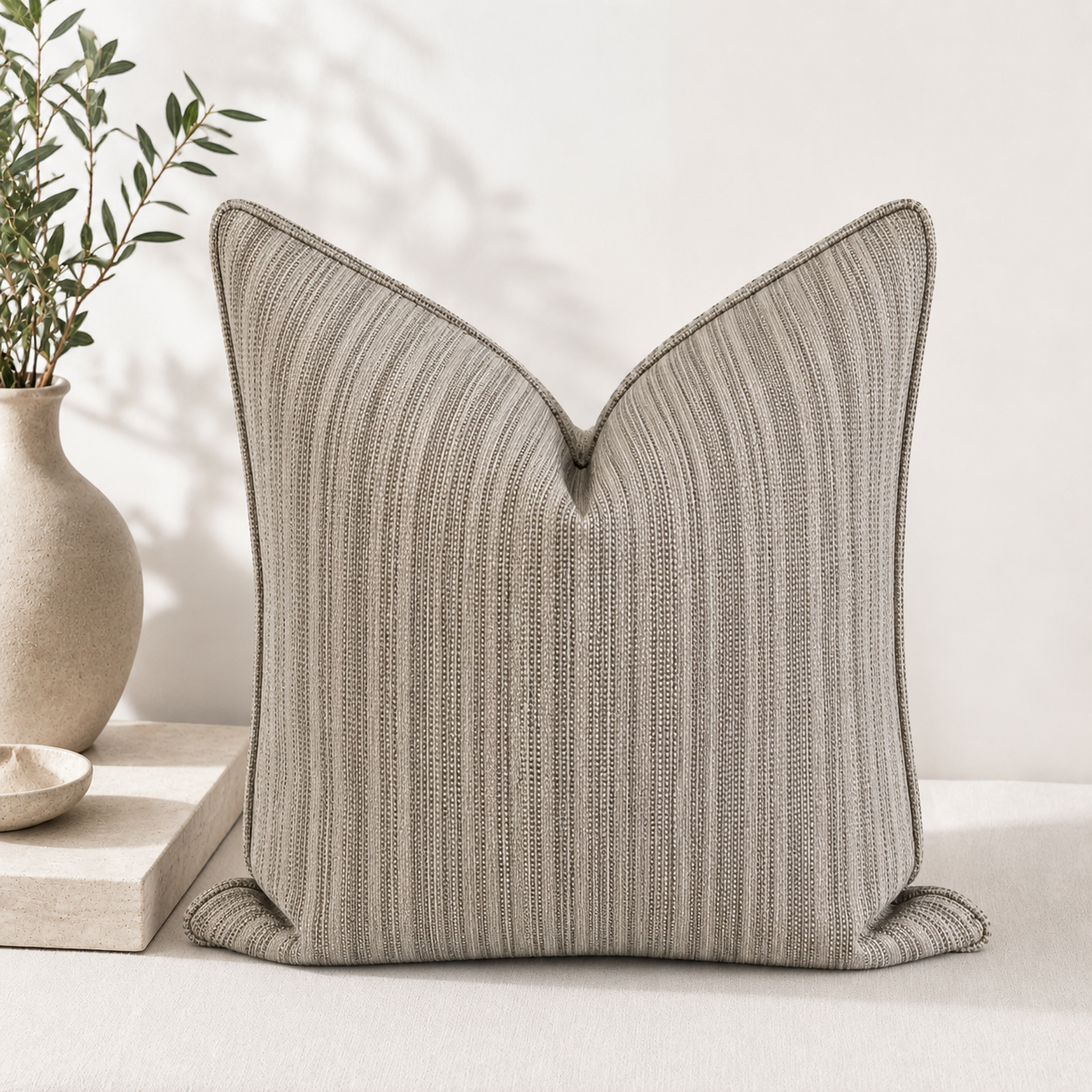 Coussin décoratif à finition valise en tissu tissé au Maroc avec fines rayures taupe et écrues, mis en scène dans un salon moderne aux tons naturels.