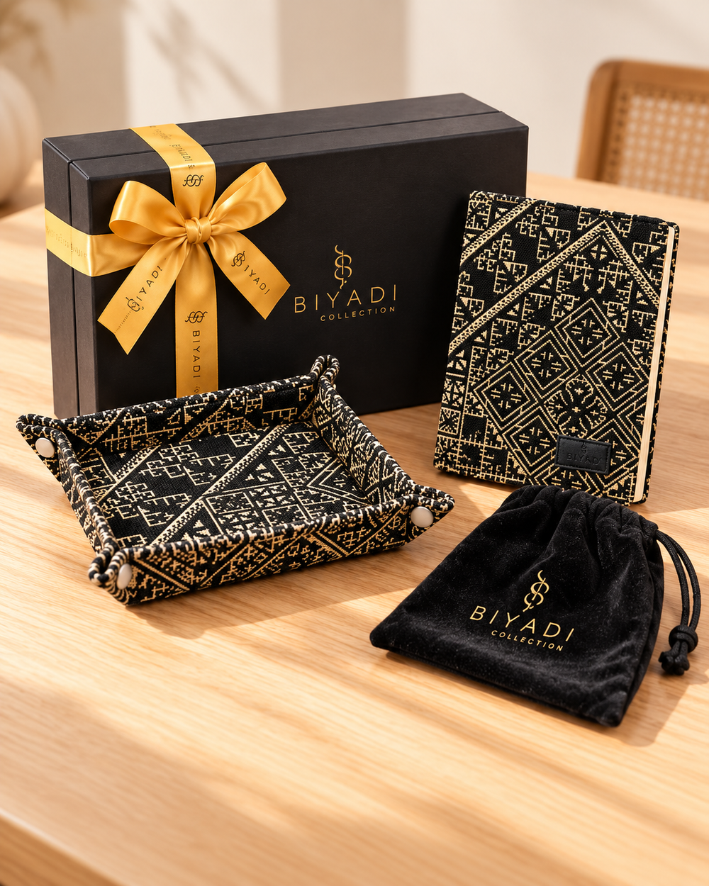 Coffret cadeau Biyadi Collection composé d’un carnet et d’un vide-poche en tissu marocain noir et écru à motifs géométriques, accompagnés d’une housse noire, d’un ruban doré personnalisé et d’une carte Biyadi, sur une table en bois clair.
