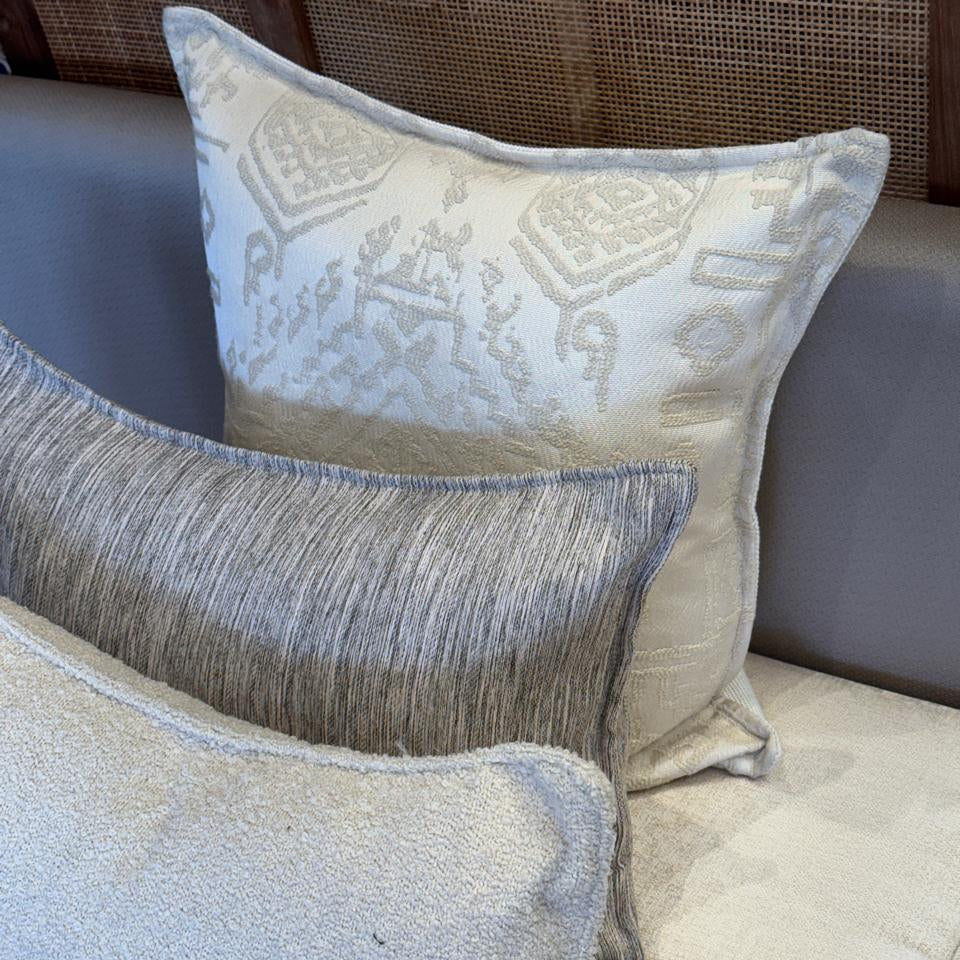 Composition de coussins décoratifs avec coussin ethnique écru tissé en relief et coussin rectangulaire gris à fines rayures, style chic et élégant.