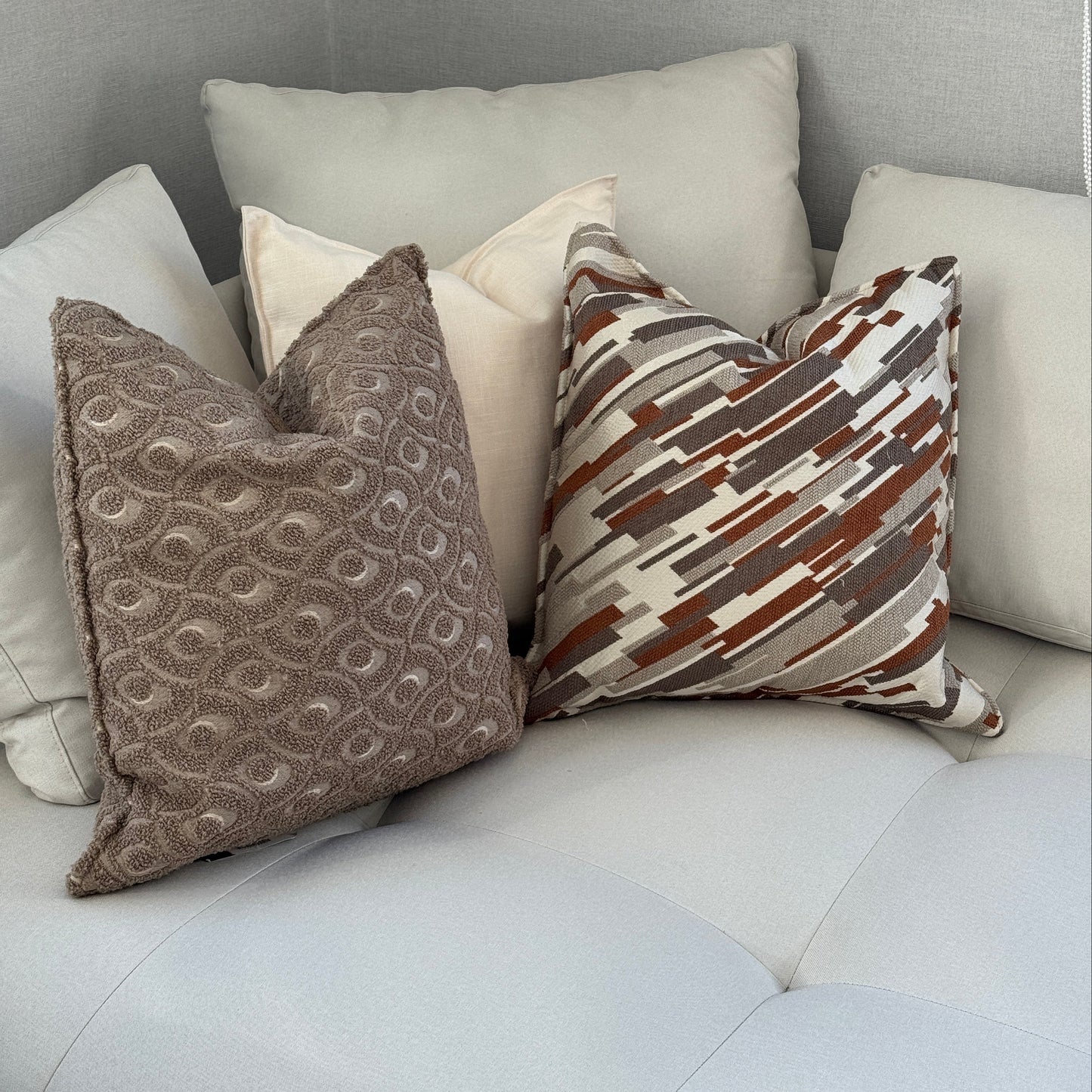 Composition de coussins décoratifs taupe, écrus et terracotta sur canapé clair dans une ambiance moderne et chaleureuse aux tons naturels.