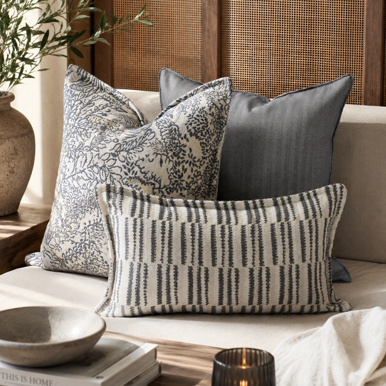 Composition de coussins décoratifs gris et beige dans un salon élégant au style moderne avec textures raffinées et ambiance chaleureuse.