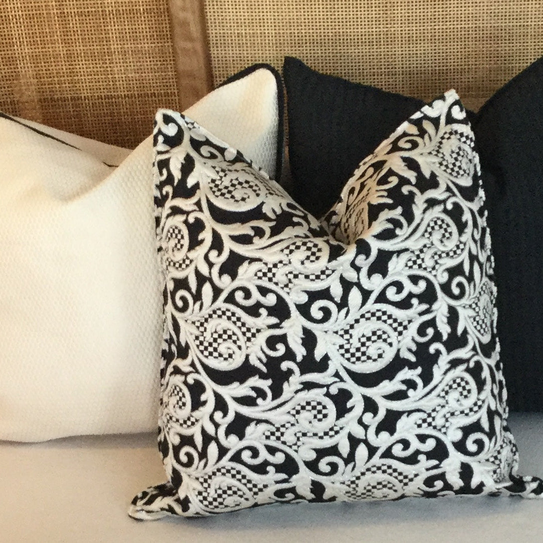 Coussin décoratif noir et écru à motif arabesque élégant posé sur un canapé clair avec coussins unis dans une ambiance moderne et raffinée.