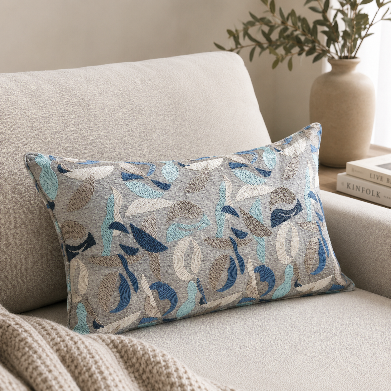 Coussin rectangulaire décoratif à motif abstrait bleu, beige et écru posé sur canapé clair dans une ambiance moderne et élégante.