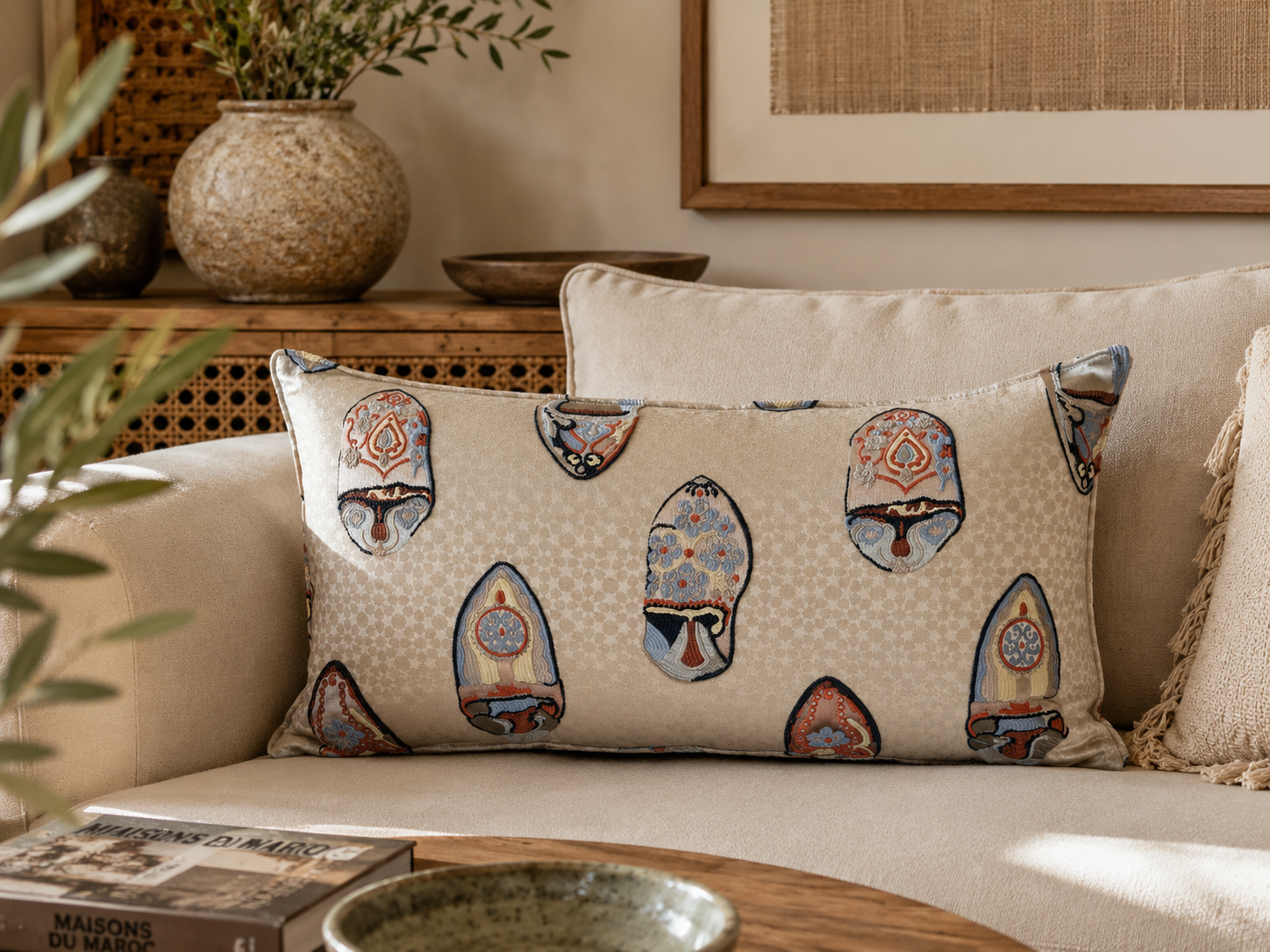 Coussin rectangulaire beige à motif babouches marocaines brodées bleu et terracotta, présenté dans une ambiance élégante et chaleureuse, création exclusive Biyadi Collection.