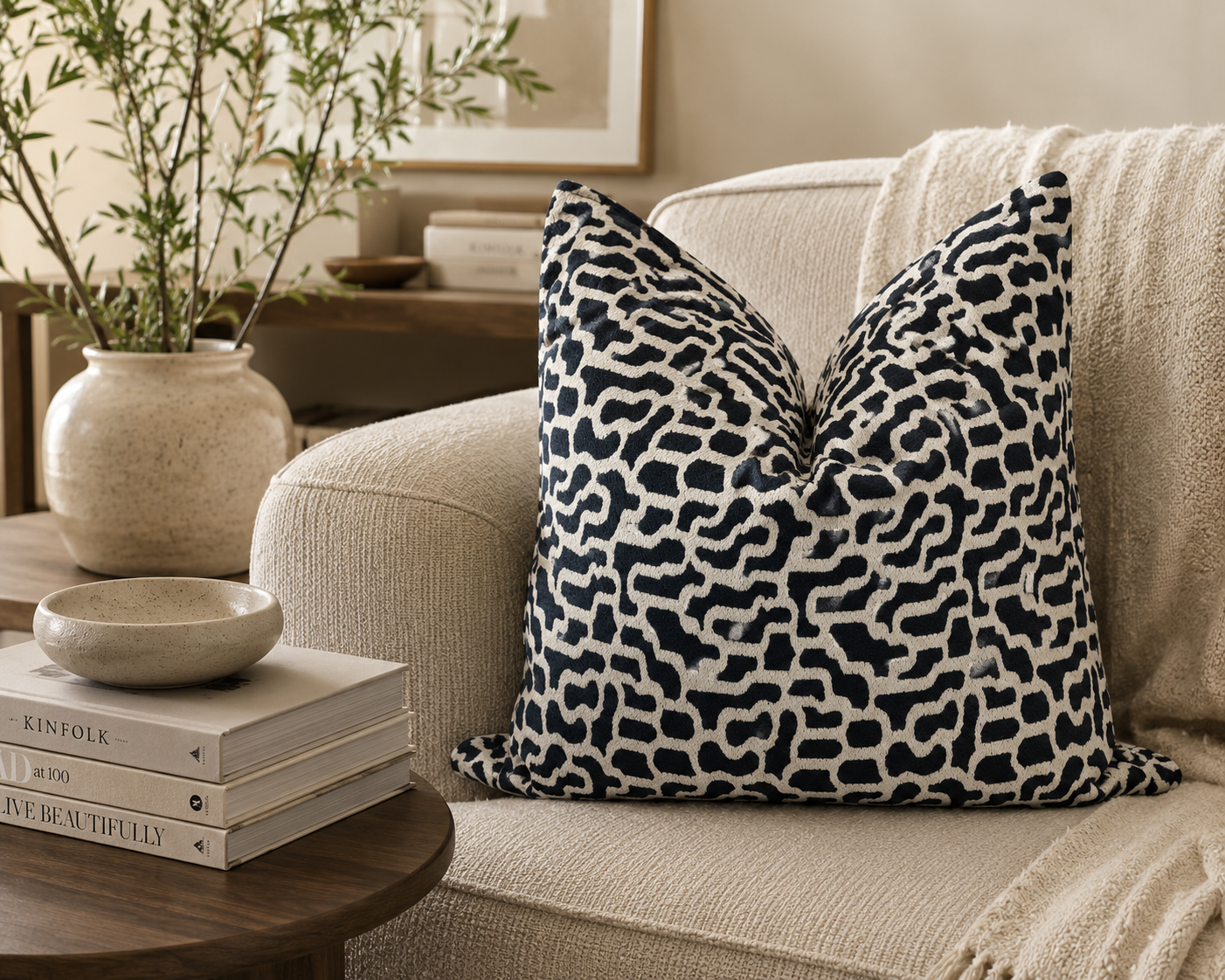 Coussin décoratif bleu et écru à motif organique posé sur un canapé beige dans une ambiance élégante et chaleureuse avec décoration minimaliste et bois foncé.
