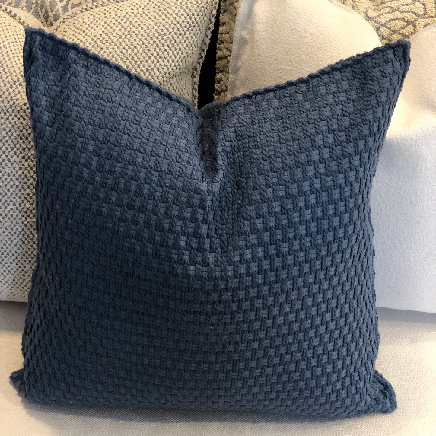 Coussin décoratif bleu  à texture tissée posé sur un canapé avec assortiment de coussins modernes aux tons neutres.
