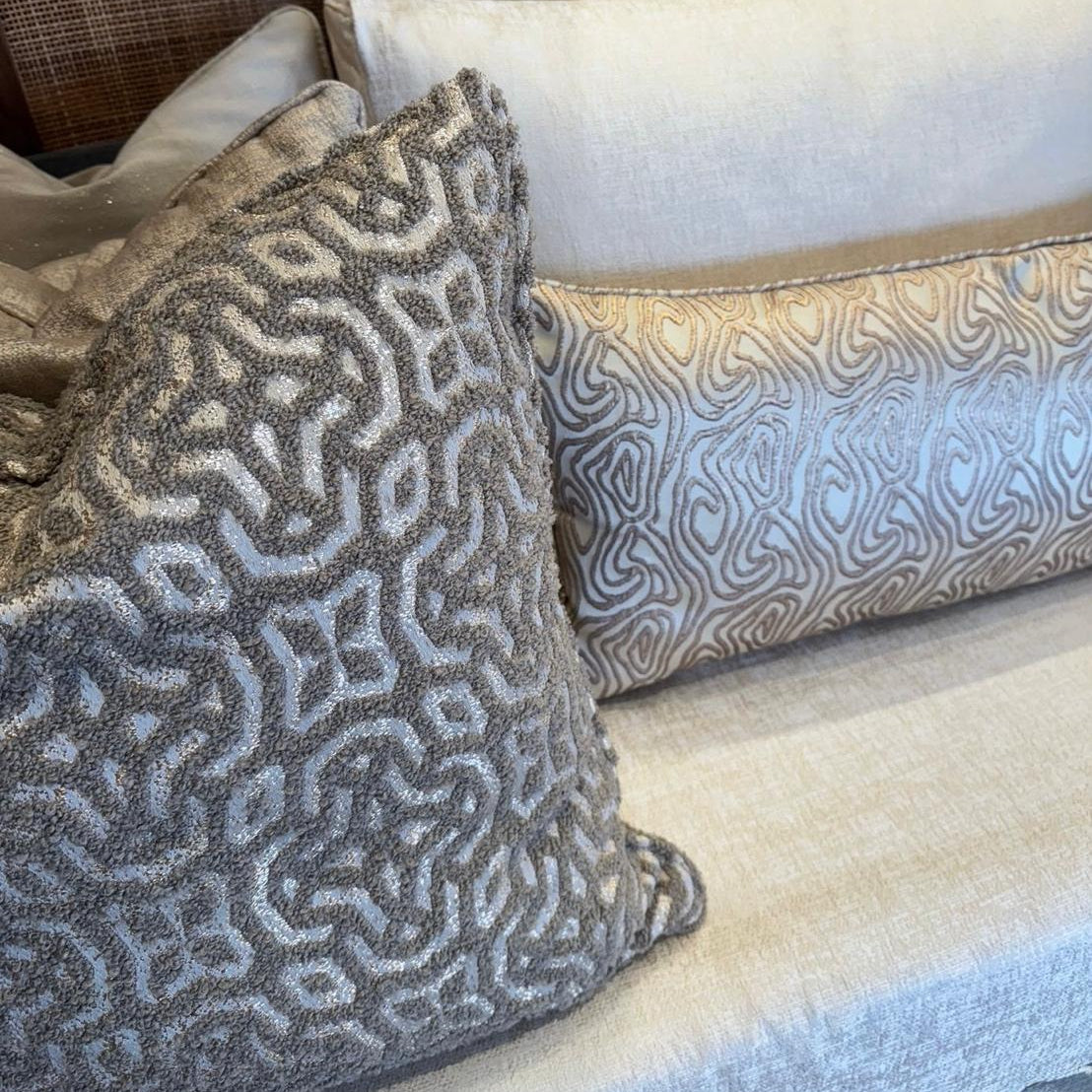 Coussin bouclette taupe à motif géométrique en relief posé sur un canapé aux tons naturels avec coussin décoratif assorti.