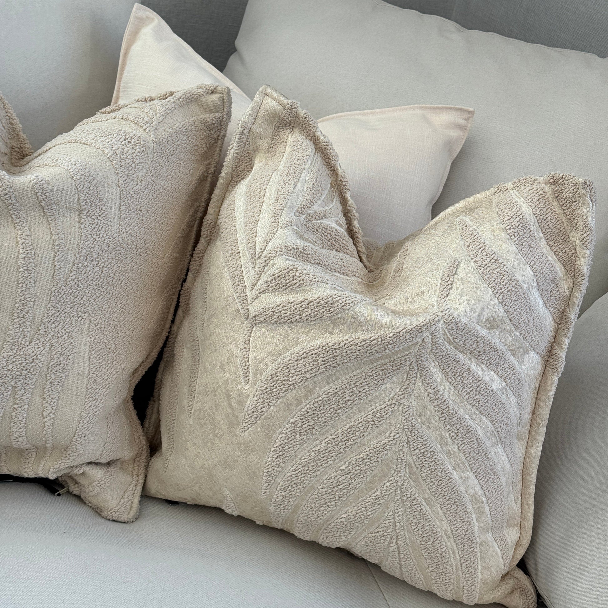 Coussins décoratifs bouclette beige à motif feuillage dans un salon élégant aux tons crème avec ambiance douce et contemporaine.