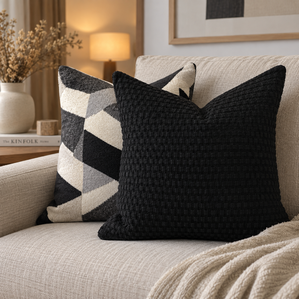 Coussin en bouclette noire 50x50 cm sur canapé beige, accompagné d’un coussin graphique noir, gris et écru.