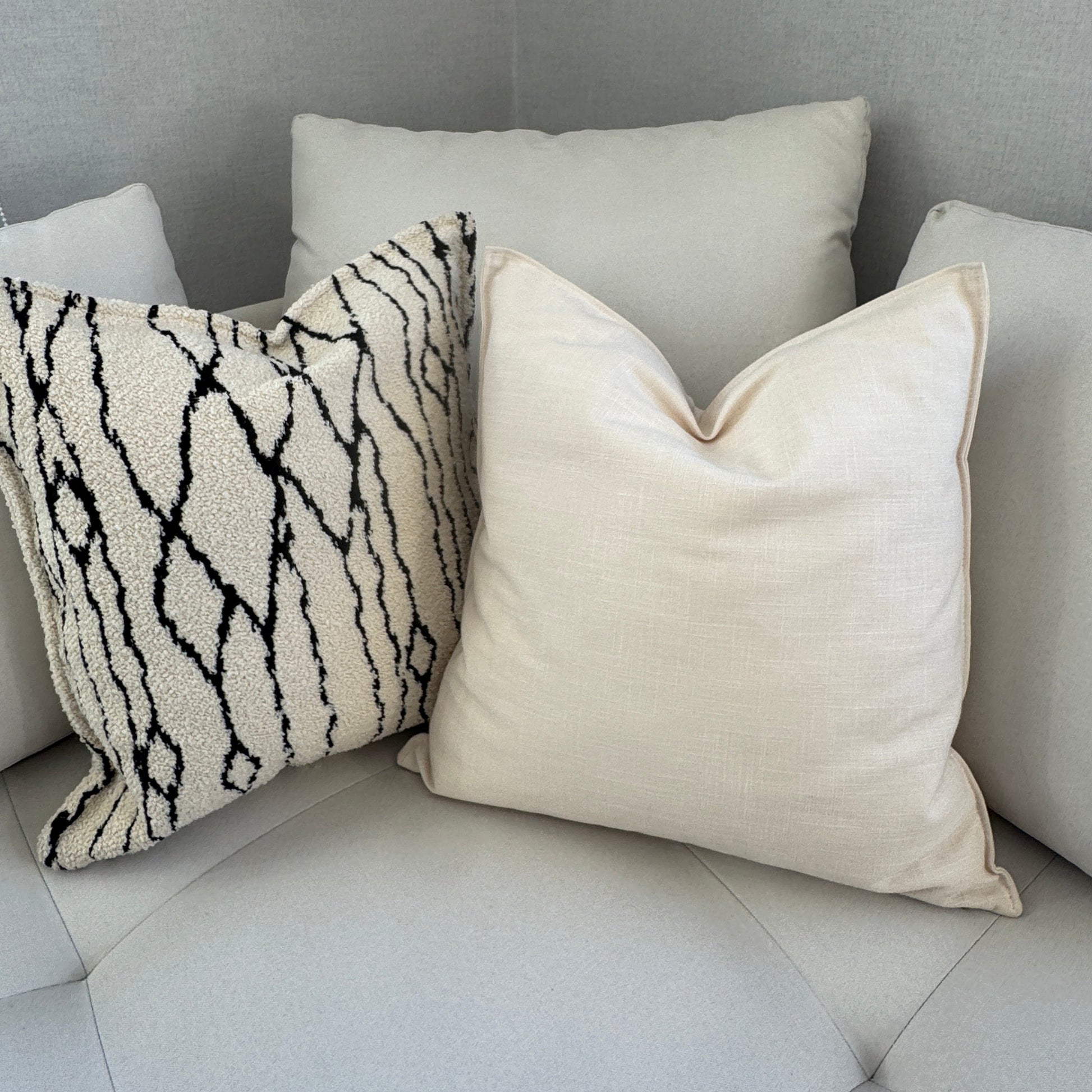 Coussin décoratif bouclette noir et blanc accompagné d’un coussin uni écru sur un canapé moderne beige clair