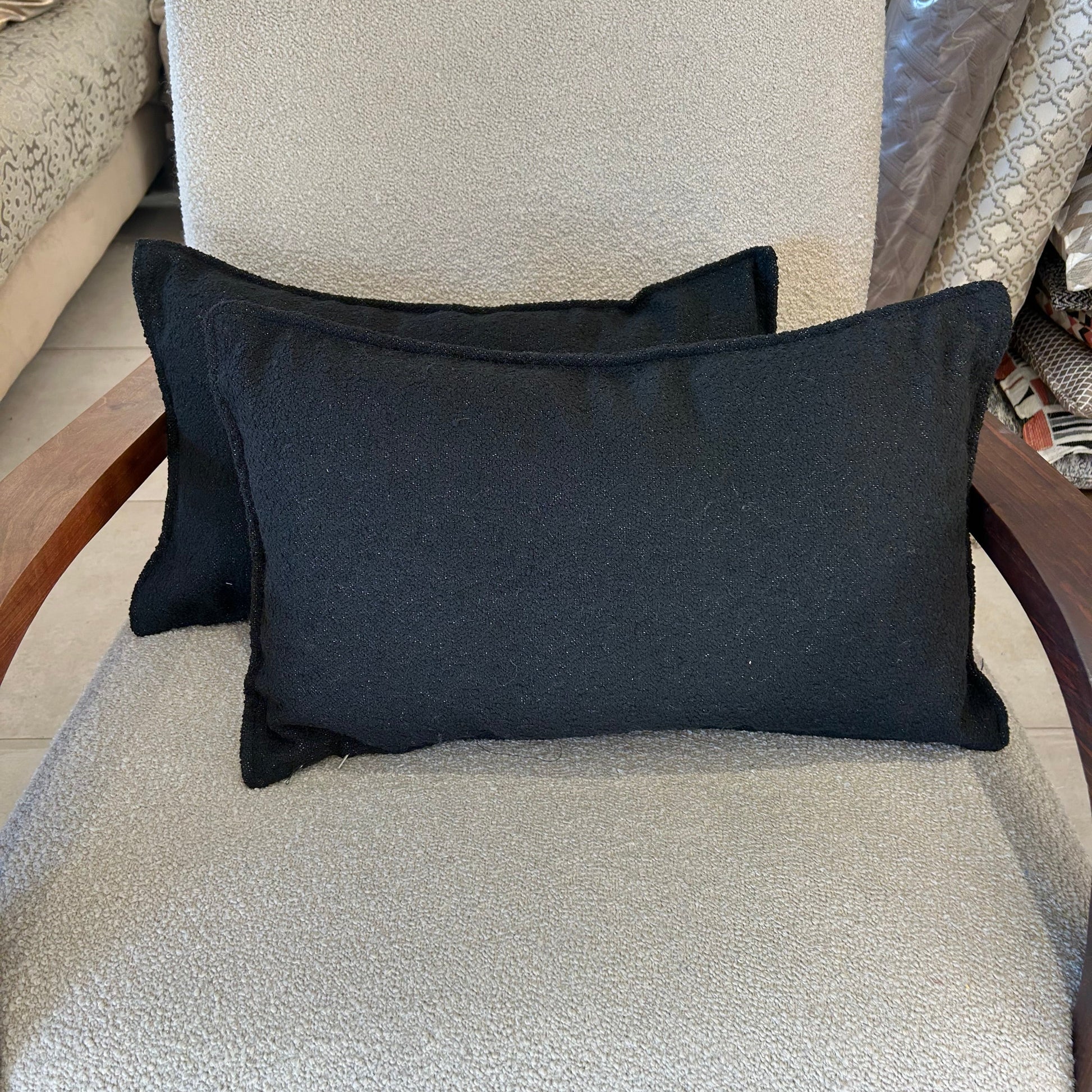 Coussins rectangulaires en tissu bouclette noir, texture douce et élégante, posé sur fauteuil clair