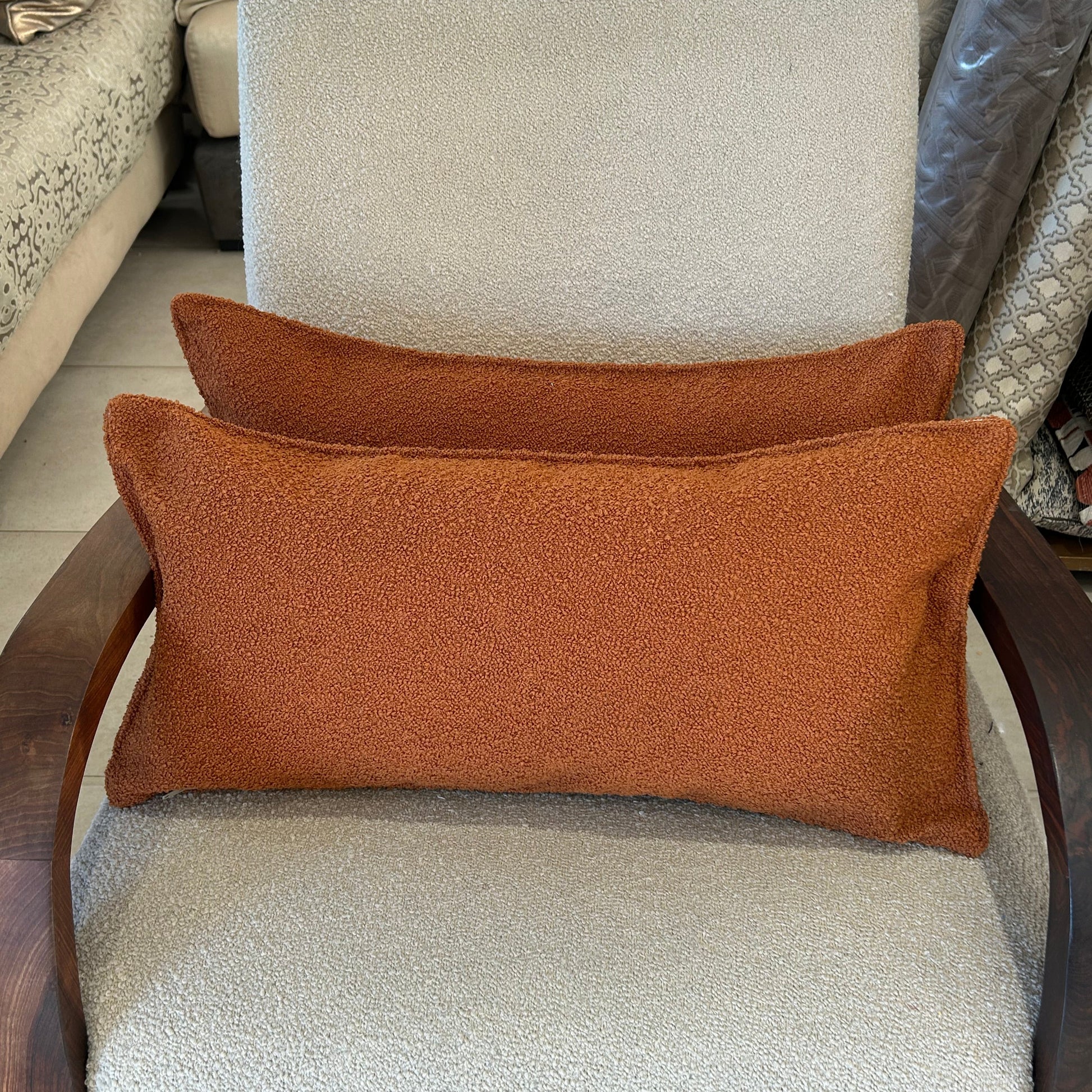 Lot de deux cousins rectangulaires en tissu bouclette terracotta, texture douce et chaleureuse, posé sur fauteuil écru