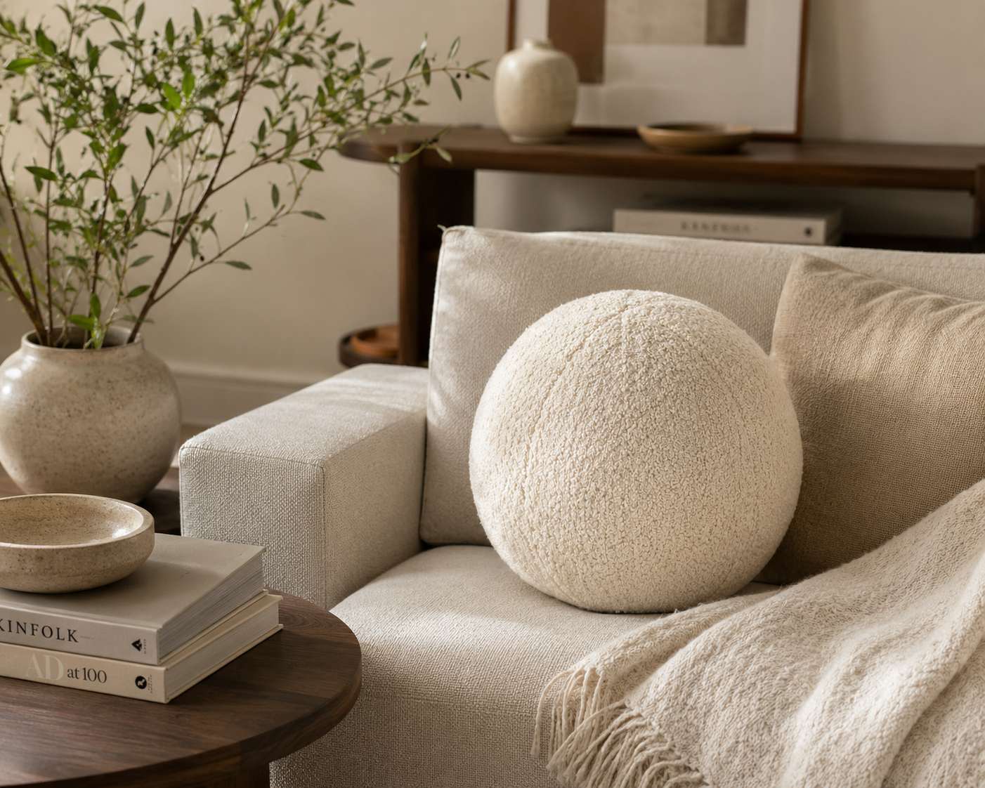 Coussin boule en bouclette écrue posé sur un canapé beige dans une ambiance chaleureuse et minimaliste avec table en bois foncé et décoration naturelle.