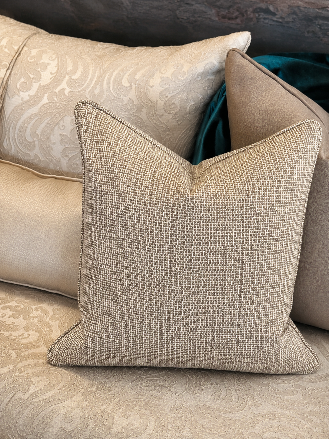 Coussin carrétaupe doré pailleté à texture tissée en tissu tissé au Maroc, mis en scène sur un canapé avec des coussins aux tons crème et taupe dans une ambiance chaleureuse et élégante.