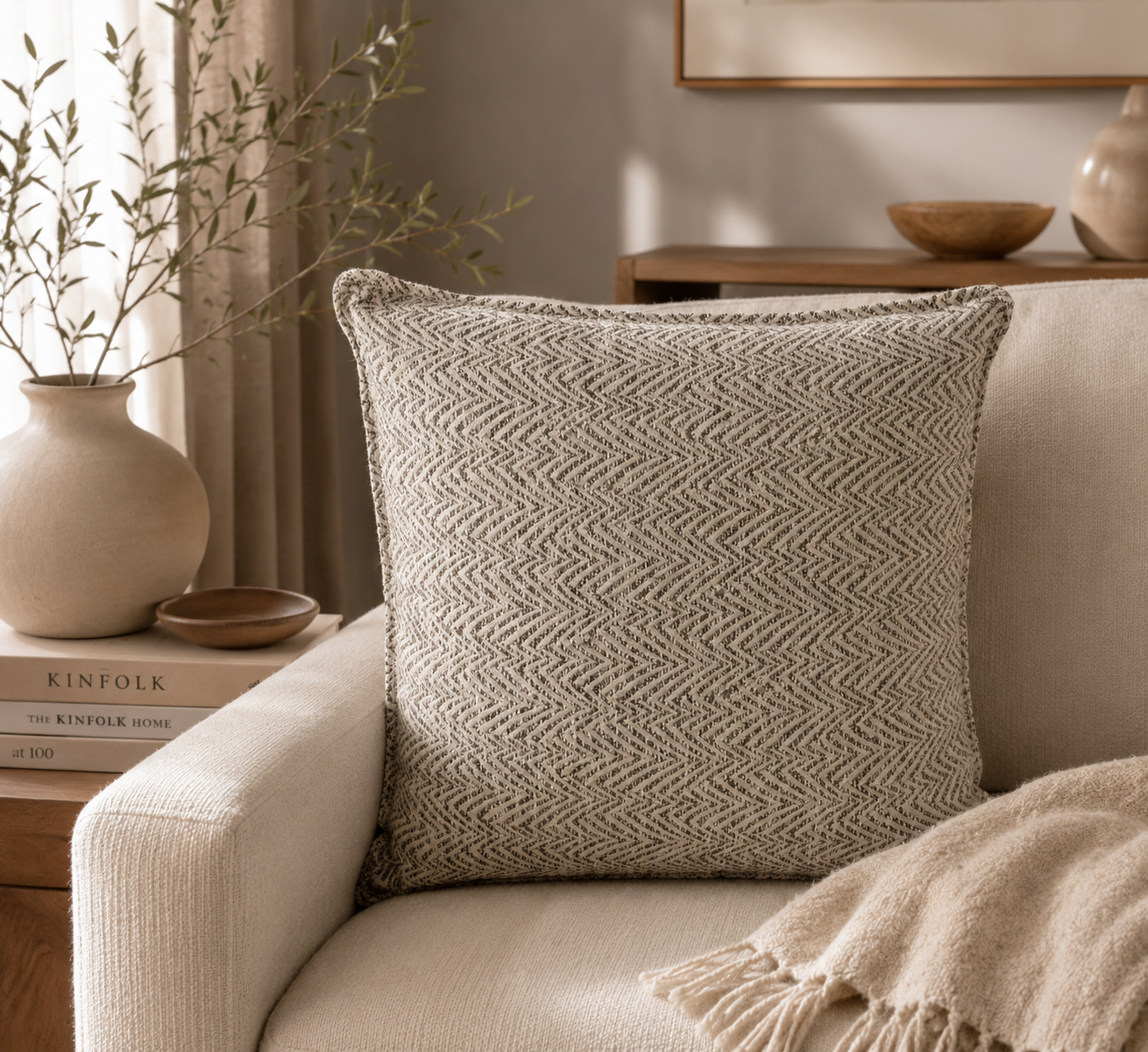 Coussin décoratif gris à motif chevron dans une ambiance chaleureuse et naturelle avec canapé clair et décoration minimaliste.
