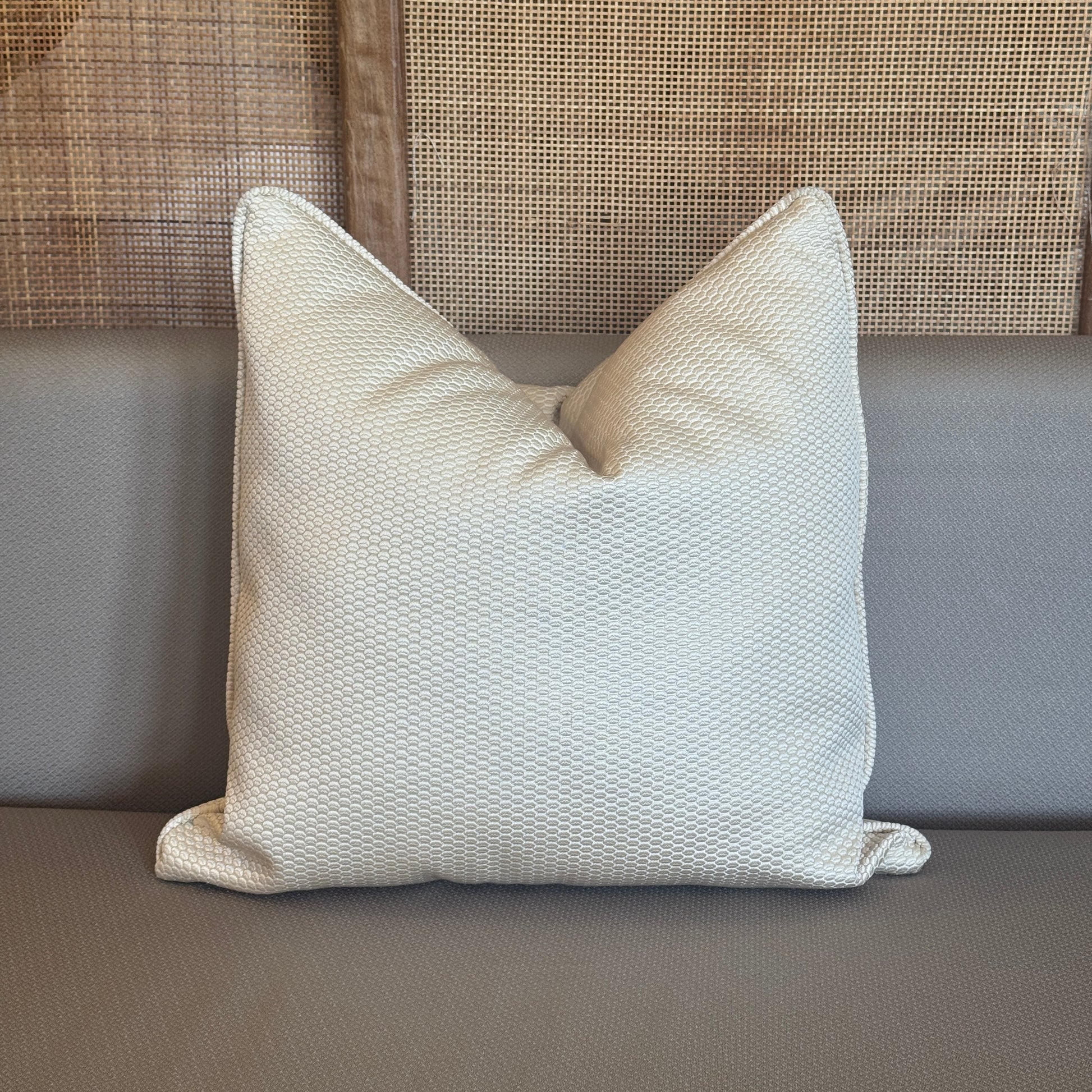 Coussin décoratif écru texturé , au style sobre et raffiné, posé sur un canapé beige dans une ambiance chaleureuse et naturelle.