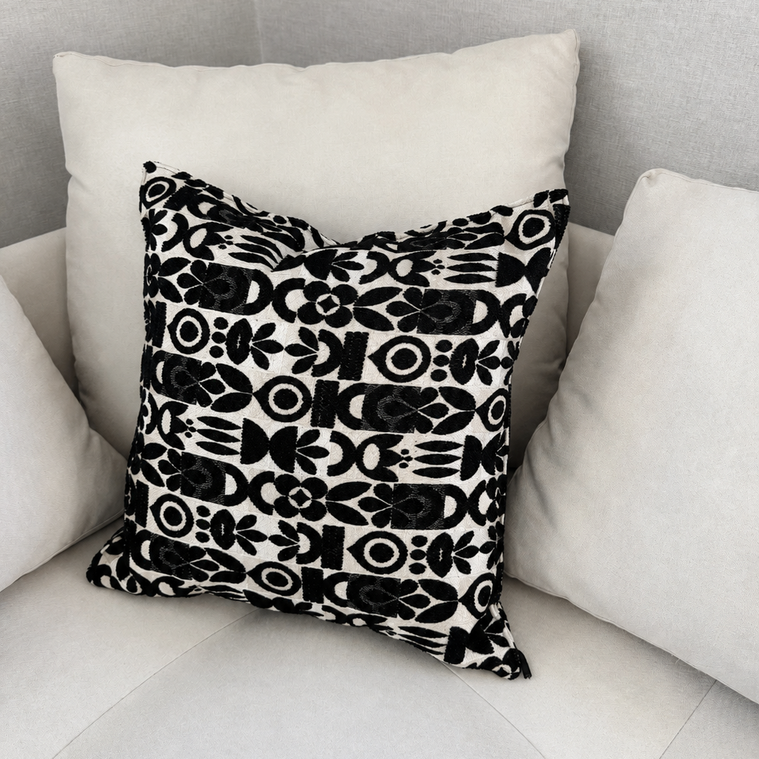 Coussin décoratif noir et blanc à motif ethnique géométrique tissé en relief, présenté sur un canapé écru. Idéal pour apporter du contraste et du caractère à un salon moderne ou contemporain.