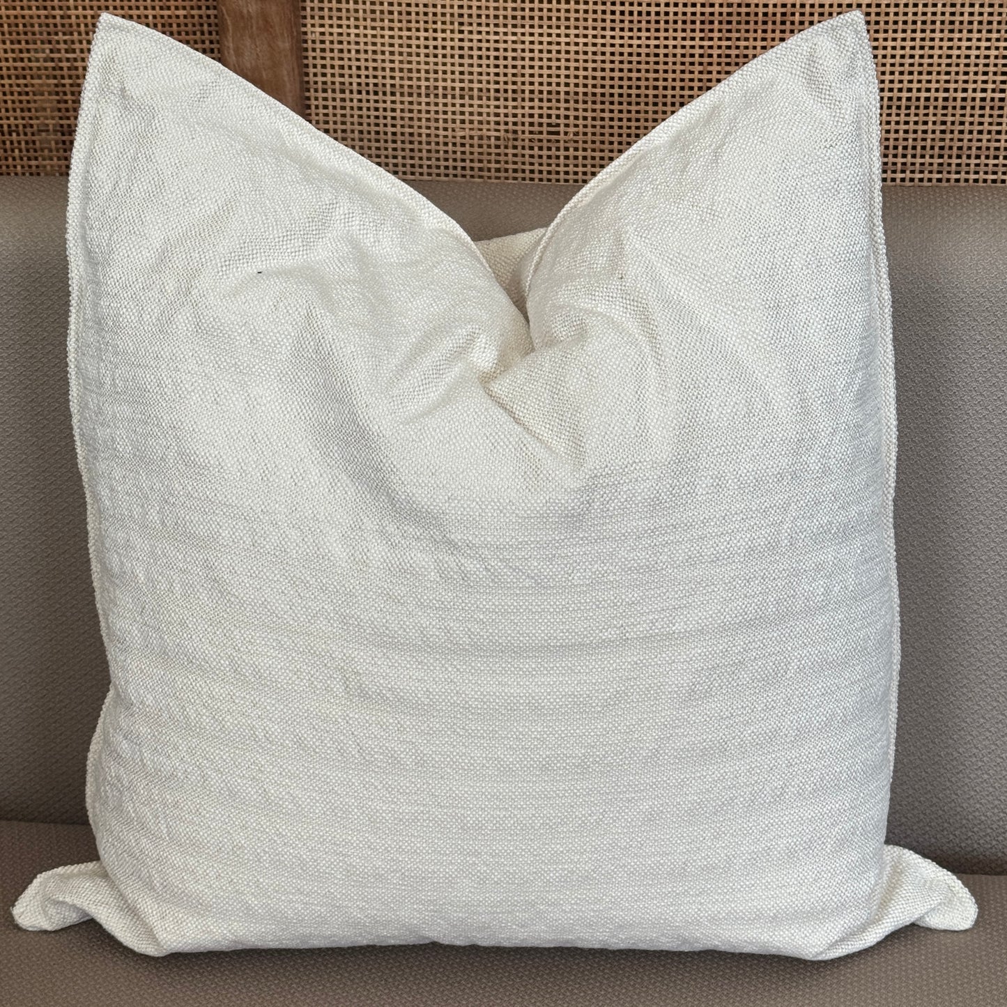 Coussin carré blanc crème avec texture tissée posé sur un canapé.
