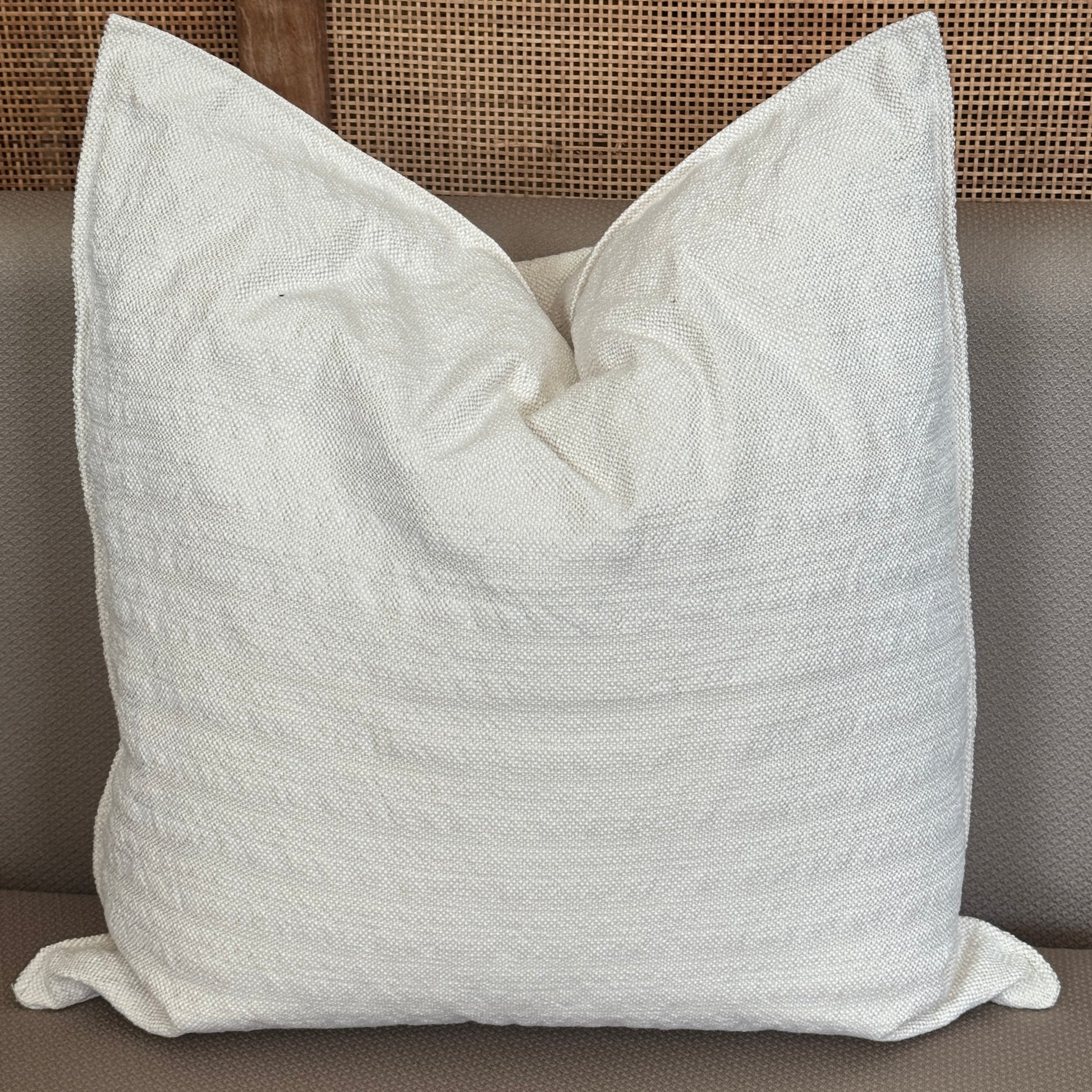 Coussin carré blanc crème avec texture tissée posé sur un canapé.