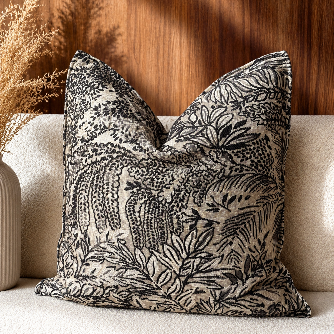 Coussin décoratif à motif feuillage noir et écru tissé au Maroc, présenté sur une assise beige dans une ambiance chaleureuse et élégante