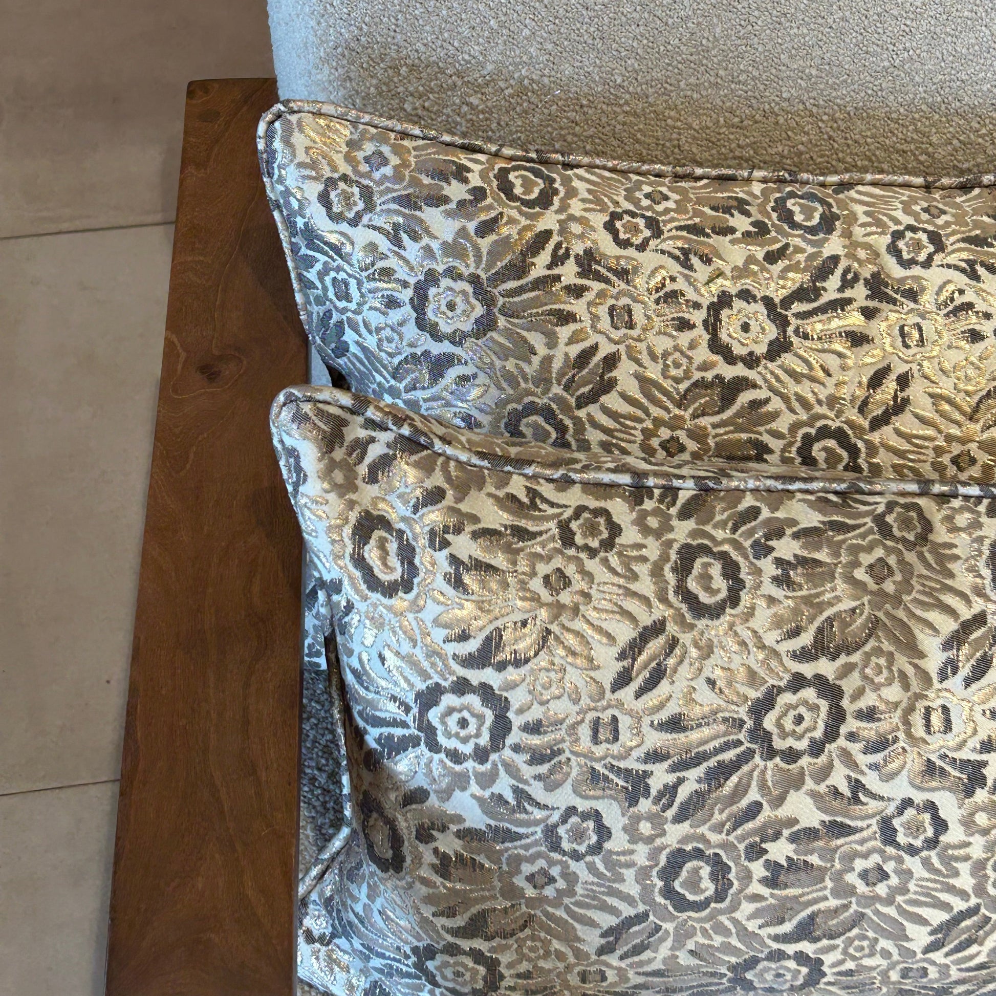 Détail de coussins rectangulaires à motif floral beige et gris en tissu texturé légèrement brillant, posés sur fauteuil clair