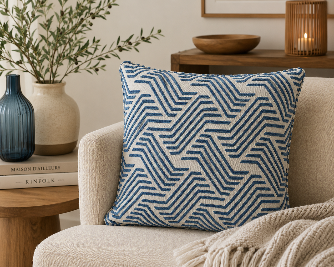 Coussin décoratif bleu et écru à motif géométrique dans une ambiance moderne et chaleureuse avec fauteuil beige, bois naturel et décoration élégante.