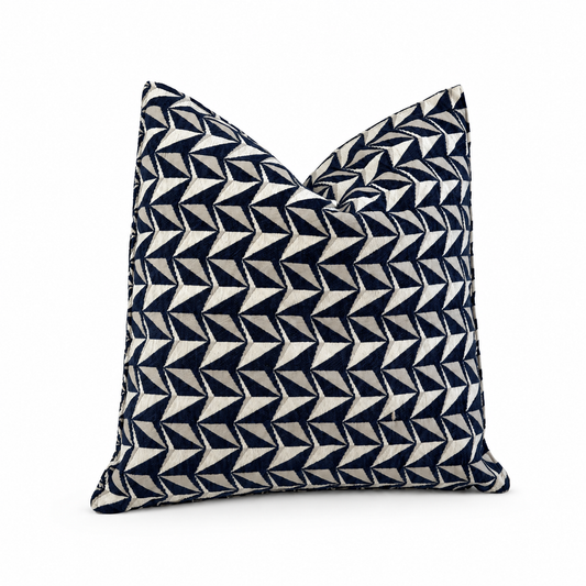Coussin décoratif bleu marine et écru à motif géométrique sur fond blanc.