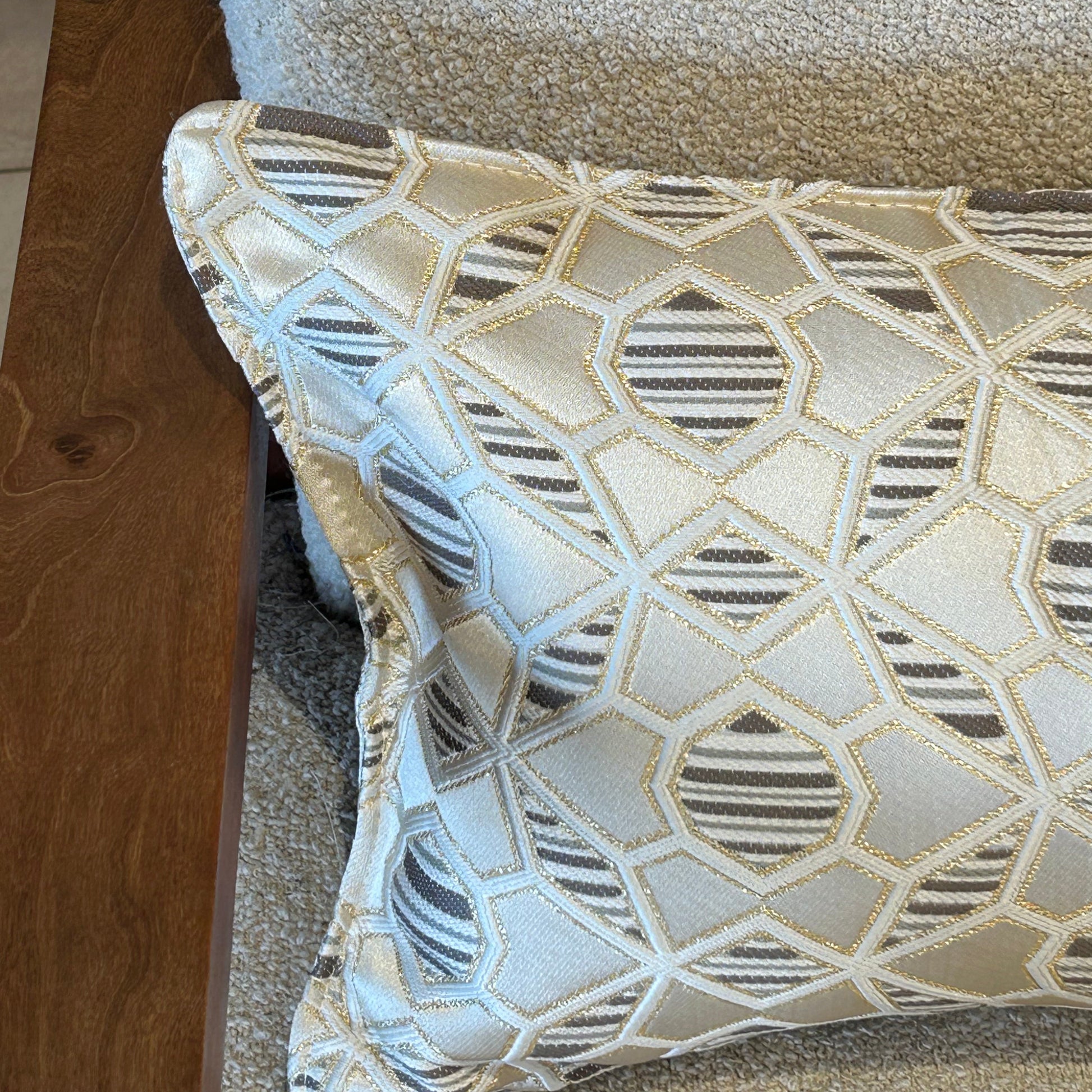 Détail d’un coussin rectangulaire à motif géométrique écru et taupe en tissu texturé, finition soignée, posé sur fauteuil clair