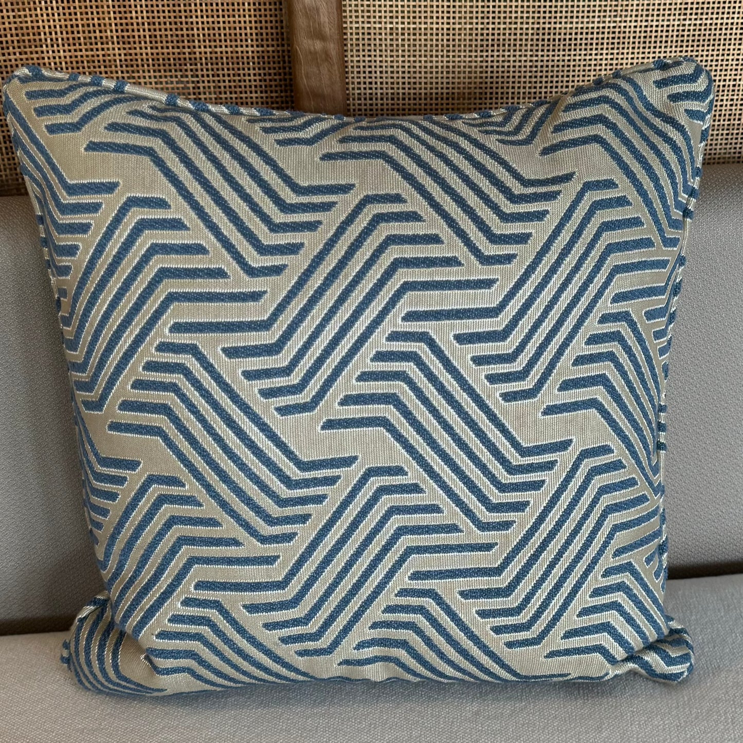 Coussin décoratif bleu et écru à motif graphique géométrique en relief sur fond blanc, style moderne et élégant pour décoration intérieure.