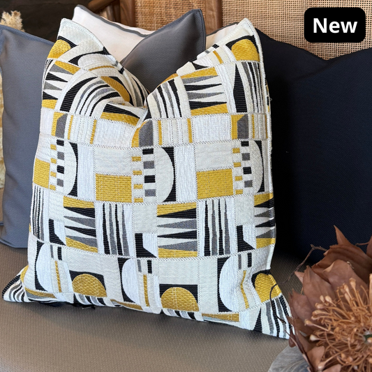 Coussin décoratif graphique jaune, gris et écru posé sur canapé contemporain clair