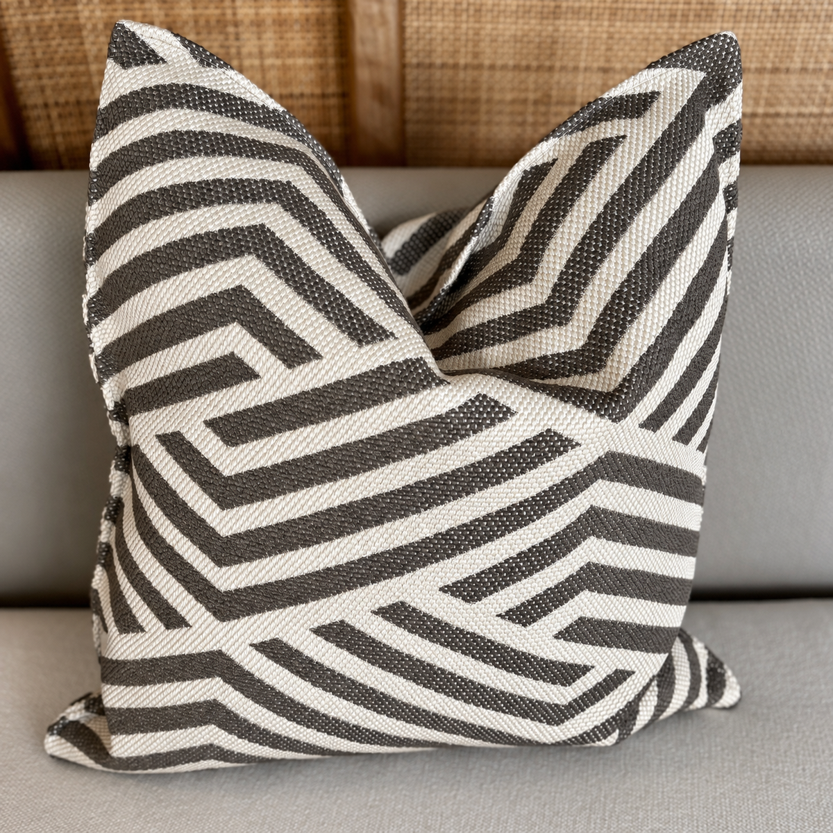 Coussin décoratif graphique taupe et écru à motif chevron géométrique posé sur une assise beige, style moderne et élégant.