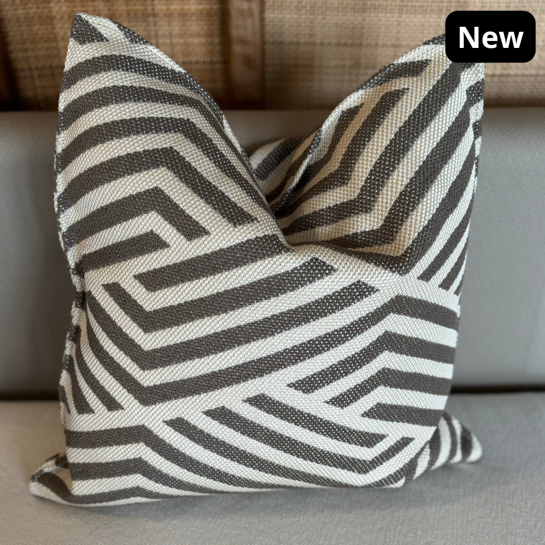 Coussin décoratif graphique taupe et écru à motif chevron géométrique posé sur une assise beige, style moderne et élégant.