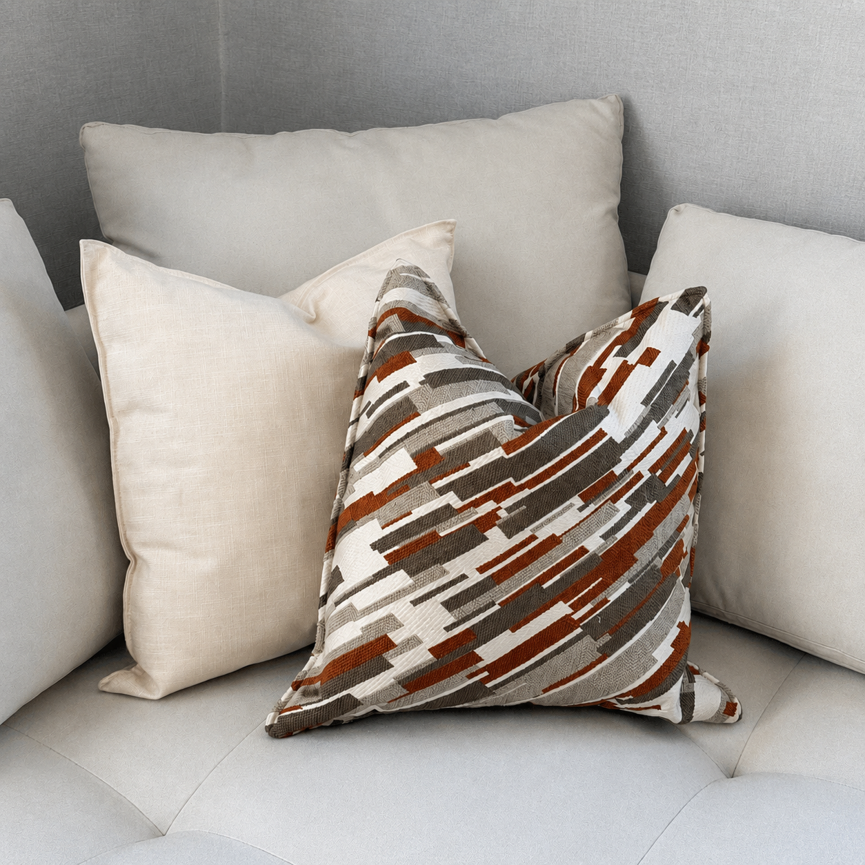 Coussin décoratif graphique terracotta, taupe et écru posé sur un canapé clair avec coussins unis dans une ambiance moderne et chaleureuse.