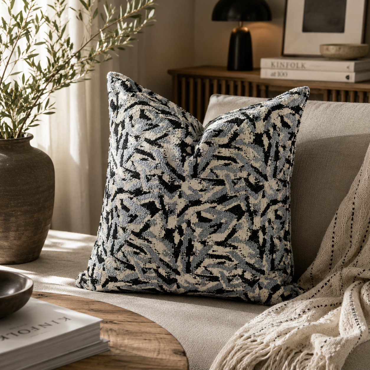 Coussin décoratif à motif abstrait gris et bleu dans une ambiance moderne et chaleureuse avec canapé beige et décoration naturelle.