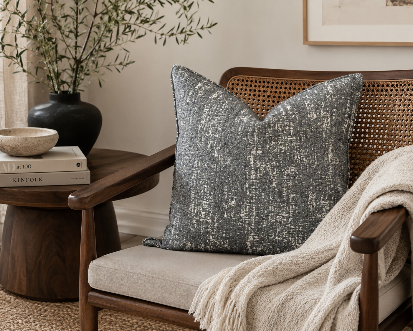 Coussin décoratif grisen bouclette posé sur un fauteuil en bois foncé avec dossier en cannage dans une ambiance chaleureuse et élégante aux tons naturels.