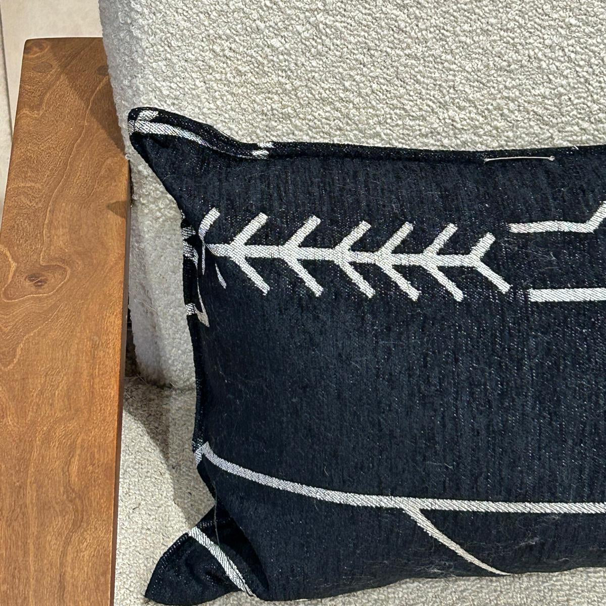Détail d’un coussin rectangulaire noir à motif graphique blanc en tissu texturé, finition soignée, posé sur fauteuil clair