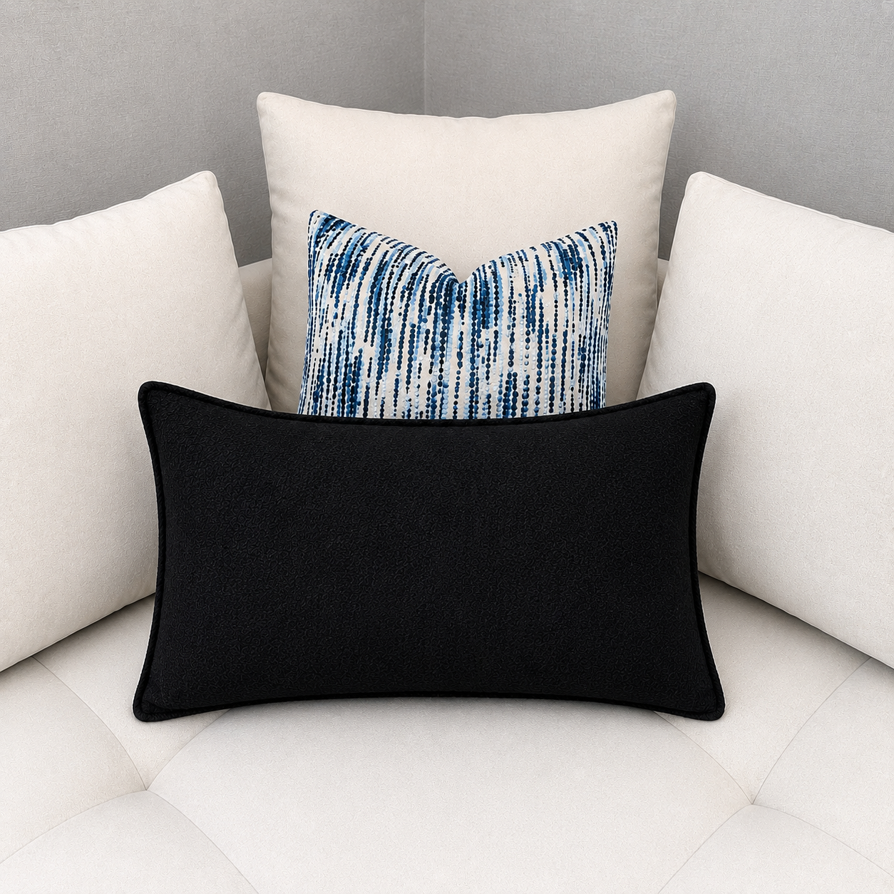 Coussin décoratif rectangulaire noir associé à un coussin graphique bleu et blanc sur canapé moderne aux tons clairs.